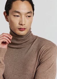 Brauner gerippter Rollkragenpullover mit langen Ärmeln, weicher Textur, tailliertem Design, hohem Kragen und dezenten Nähdetails.