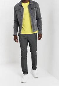 Grå denimjakke over en lys gul T-shirt, parret med mørkegrå bukser og hvide sneakers, der har en afslappet pasform og rene linjer.
