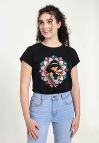 Sort bomulds-t-shirt med en farverig grafik af en karakter omgivet af blomster mønstre, parret med lyseblå højtaljede jeans.