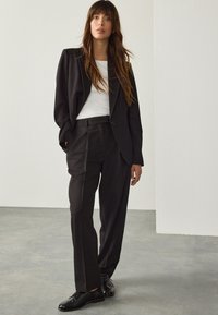 Costume noir avec blazer ajusté et pantalon taille haute, accompagné d'un haut blanc côtelé. Tissu doux et coupe décontractée, avec des chaussures à lacets.