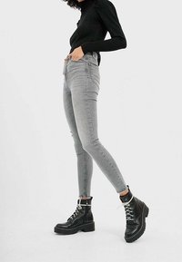 Úzké šedé džíny vyrobené z denimu, s poloviční výškou pasu. V kombinaci s černými combat botami s bílými tkaničkami a strukturovanou platformou.