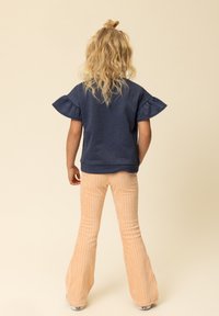 Marineblauwe pullover met gerafelde mouwen, gecombineerd met licht perzikkleurige corduroy flared broek met verticale strepen. Geschikt voor casual gebruik.