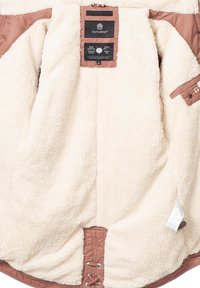 Beige hoodie met een zachte, fluffy binnenkant, voorzien van een bruine buitenkant, een trekkoordsluiting en merktekens aan de binnenkant.