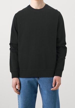 Sudadera negra de manga larga, con diseño de cuello redondo y puños acanalados. Combinada con jeans de mezclilla azul claro. Material de algodón ligero.