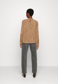 Blusa bege com padrão de pintas, detalhe de abertura em forma de chave nas costas e mangas longas, combinada com calças cinza de cintura alta e sapatos de salto pretos.