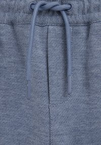 Primer plano de tela de mezclilla azul con una pretina y dos cordones a juego pasados por ojales metálicos.