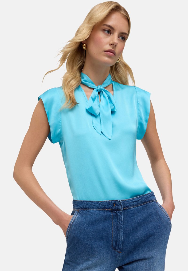 Blusa senza maniche di colore azzurro chiaro con dettaglio del collo annodato. Realizzata in tessuto morbido, presenta una vestibilità comoda e un decolté a V.