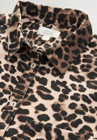 Chemise à boutons imprimé léopard en beige clair et noir, dotée d'un col classique, de deux boutons et d'une poche poitrine, confectionnée en lin.