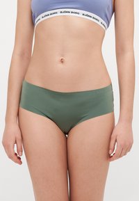 Mutande hipster verdi senza giunture con una finitura liscia e opaca. Presentano un taglio basso e un design minimalista. Elastico in vita con logo del marchio.