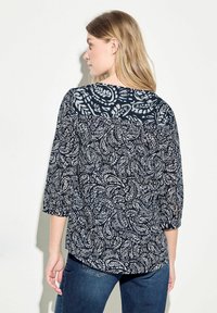 Blusa blu navy con maniche a ¾, caratterizzata da un motivo paisley in azzurro chiaro e bianco. Tessuto testurizzato, scollatura tonda e vestibilità ampia.