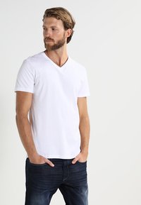 Weißes Baumwoll-T-Shirt mit V-Ausschnitt und kurzen Ärmeln, kombiniert mit dunkelblauen Jeans. Glatte Textur und normale Passform; lässiges Design ohne Muster.