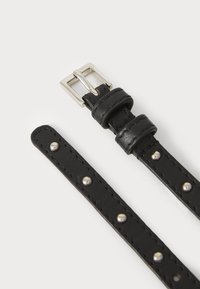 Correa de cuero negro con hebilla y tachuelas plateadas, con bordes cosidos y una textura suave, diseñada para un ajuste seguro.