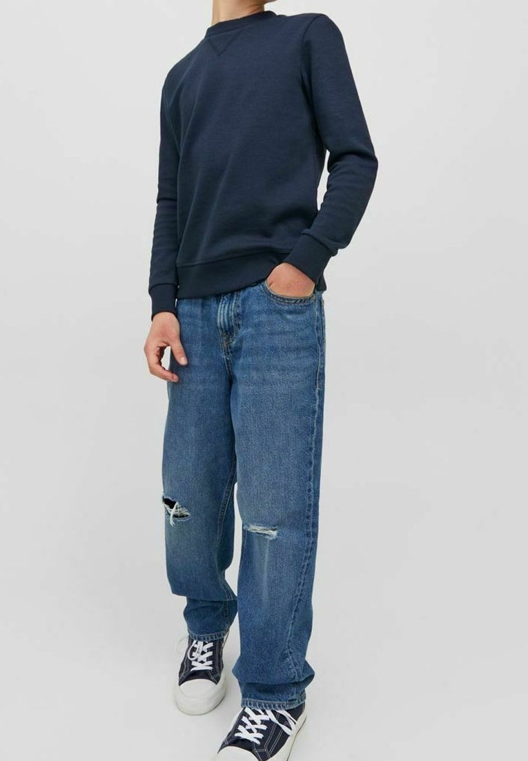 Marinblå sweatshirt med ribbad mudd, kombinerad med ljusblå slitna jeans. Jeansen har revor vid knäna, bärs med marinblå sneakers.