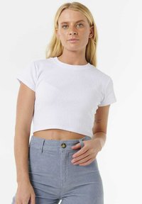 T-shirt bianca corta in tessuto a coste con maniche corte. Abbinata a pantaloni in velluto a coste azzurri chiari con bottone frontale e tasche.