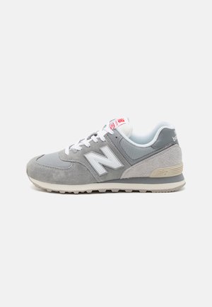 Gray sneakers with a mix of suede and mesh, featuring a white "N" logo, white laces, and a beige rubber sole. Additional red accents on the tongue.