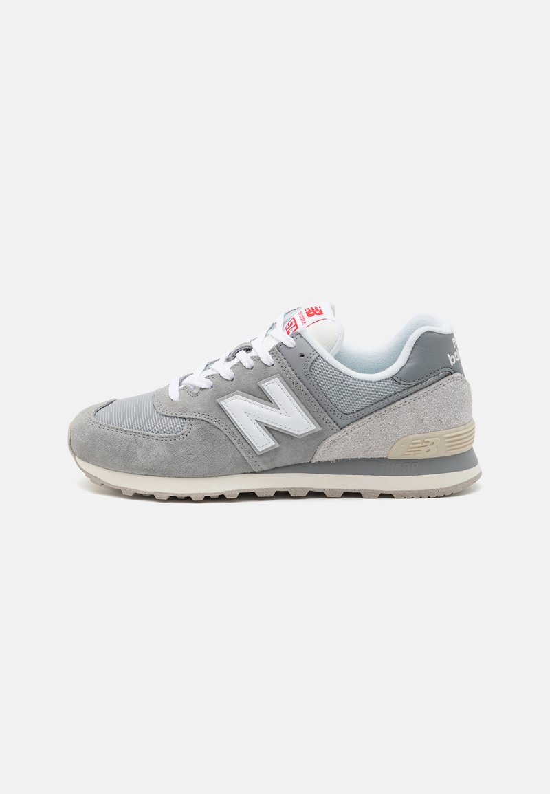 Gray sneakers with a mix of suede and mesh, featuring a white "N" logo, white laces, and a beige rubber sole. Additional red accents on the tongue.