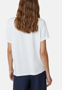 T-shirt bianco a maniche corte con una texture morbida, vestibilità relaxed e orlo dritto. Indossato con pantaloni fantasia blu navy, visto da dietro.