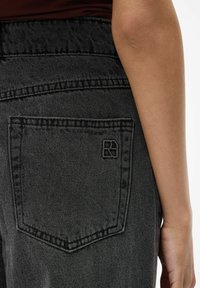 Schwarze Jeans aus Denim mit strukturierter Oberfläche, ausgestattet mit einer Gesäßtasche mit gesticktem Rand und eingeprägtem Markenlogo.