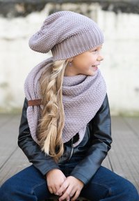 Lavendel gebreide beanie en sjaal, met textuur en slouchy stijl, gecombineerd met een zwarte leren jas. Lange gevlochten haren accentueren de outfit.