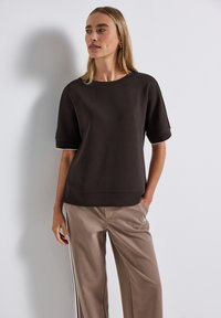 Bruine top met korte mouwen van een zachte stof, met een ronde hals en witte accents. Gecombineerd met beige broek met zijstrepen.