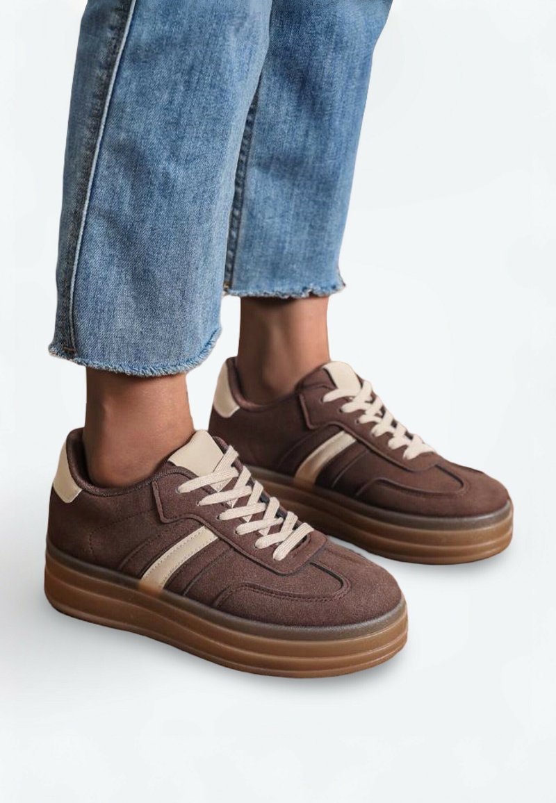 Baskets en daim marron avec des accents beiges, semelle en caoutchouc épaisse et lacets crème. Présentent un design épuré et une tige texturée. Poignets en denim visibles.
