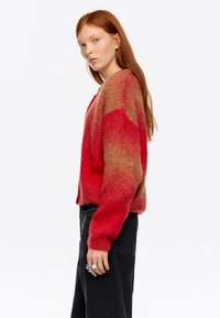 Sweter w czerwono-brązowym gradiencie wykonany z miękkiego, puszystego materiału; luźny krój z opuszczonymi ramionami. Połączony z czarnymi, wysokim stanem spodniami i pierścionkami.