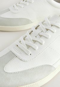 Baskets blanches en cuir texturé et en daim, avec des lacets blancs, un design classique basse et une semelle en caoutchouc avec un motif de bande de roulement subtil.