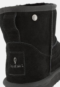Stivaletto in suede nero con texture liscia, dettagli cuciti, patch con logo e suola in gomma nera.