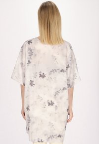 Lysfarvet oversized skjorte med løs pasform, prydet med et blomstermønster i grå nuancer og korte ærmer, lavet af blødt stof.