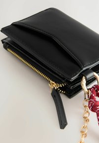 Black leather wallet with gold zipper, chain attachment, and a textured surface. Features a flap closure and multiple compartments for organization.