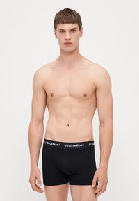 Schwarze Baumwoll-Boxershorts mit einem Logo-Bund, ausgestattet mit einem fitted Design und glatter Textur. Modell vor neutralem Hintergrund gezeigt.