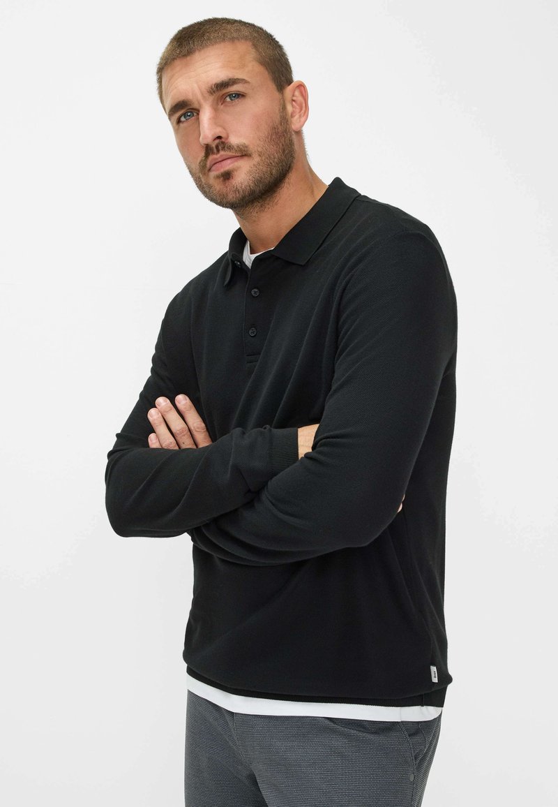 Polo shirt nero a maniche lunghe in materiale testurizzato, con colletto classico, patta con tre bottoni e un'etichetta del marchio discreta sull'orlo.