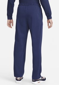 Námořnické modré tepláky s elastickým páskem, rovnými nohavicemi a bočními kapsami; nošeny s vzorovanými teniskami s bílými podrážkami.