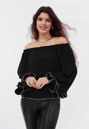 Blusa nera off-the-shoulder con maniche a volant e profili bianchi. Realizzata in tessuto leggero, presenta una vestibilità ampia e un colletto elasticizzato.