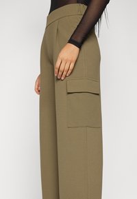 Olive green wide-leg pants with a high elastic waistband and a side cargo pocket. Fabric has a smooth texture and tailored design.