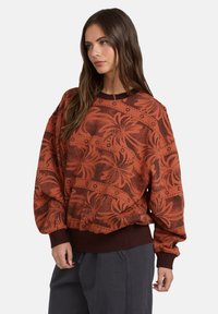Sweter w kolorze rdzy z wzorem liści palmowych, z okrągłym dekoltem i ściągaczami. Miękka tkanina o luźnym kroju.