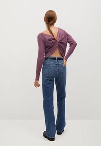 Maglione viola a coste con schiena aperta e dettaglio annodato al centro, abbinato a jeans blu a vita alta e calzature nere.