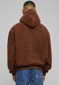 Rudas pūkuotas džemperis su tekstūru ir kapišonu. Rankogaliai ir apačia yra raištiniai. Pora - mėlynos džinsinės kelnės su siuvinėjimo detalėmis.