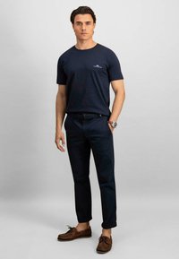 Tricou din bumbac de culoare bleumarin, cu mâneci scurte, asortat cu pantaloni închisi la culoare și pantofi de tip boat de culoare maronie. Prezintă un mic logo pe tricou.