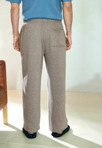 Szare, teksturowane spodnie dresowe o luźnym kroju, z elastycznym paskiem w talii i kieszenią z tyłu, w połączeniu z czarnymi kapciami.