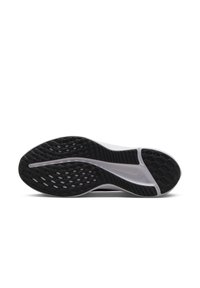 Semelle d'une chaussure de sport noir et blanc avec des motifs de grip texturés et un logo Swoosh Nike central visible.
