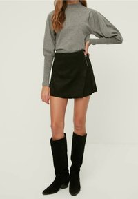 Pull gris à manches bouffantes, associé à une mini jupe noire en daim synthétique dotée d'une fermeture éclair latérale, et des bottes noires à talons hauts jusqu'aux genoux.