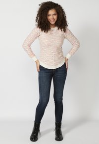 Pull en tricot rose clair avec un motif de vagues texturé, encolure ronde côtelée et poignets côtelés, associé à un jean skinny noir et des bottes à lacets noires.