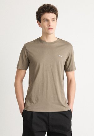 T-shirt à manches courtes et col rond en tissu taupe avec une texture lisse. Il présente un petit logo blanc "HUGO" sur la poitrine.