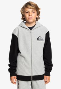 Grijze en zwarte rits-hoodie van zacht materiaal, met een kangoeroe-jaszak, een verstelbare capuchon en het Quiksilver-logo op de borst.
