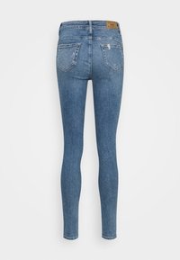 Vaqueros ajustados de mezclilla azul con bolsillos traseros, cintura alta y una textura sutilmente descolorida, con una etiqueta de marca color canela en la parte trasera.