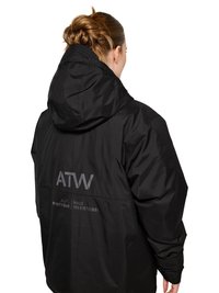 Frau mit zu einem Dutt gebundenem Haar, die eine schwarze Kapuzenjacke mit dem Schriftzug "ATW" und "OFF DUTY GEAR HALO" auf dem Rücken trägt und von der Kamera wegschaut.