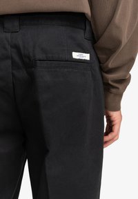 Čierne bavlnené nohavice s zadnou vreckom, na ktorom je obdĺžniková biela nálepka s nápisom "ELEMENT SKATEBOARD CO." Hladká textúra.