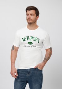 Hvid bomulds t-shirt med rund hals, med grøn "NEWPORT 1957" grafikprint og teksten "Beach Club Sporting Goods". Casual pasform.