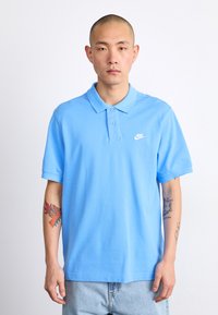 Svetlomodrá polo košela vyrobená z bavlny, s klasickým golierom, krátkymi rukávmi a malým bielym logom Nike na hrudi.